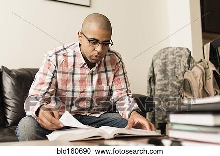 Stock Image - Mixed race soldier reading book on living room sofa. Fotosearch