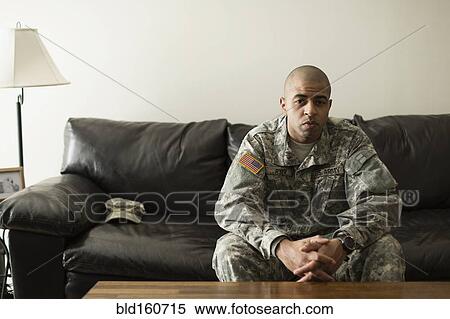 Stock Photography - Mixed race soldier sitting on living room sofa. Fotosearch