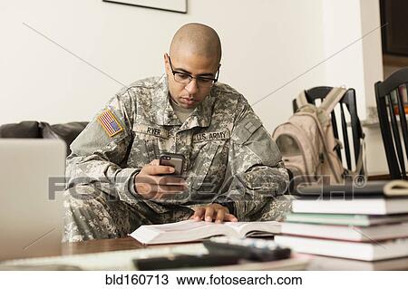 Stock Image - Mixed race soldier texting on cell phone and studying on sofa. Fotosearch