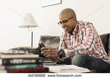 Stock Image - Mixed race soldier texting with cell phone on sofa. Fotosearch