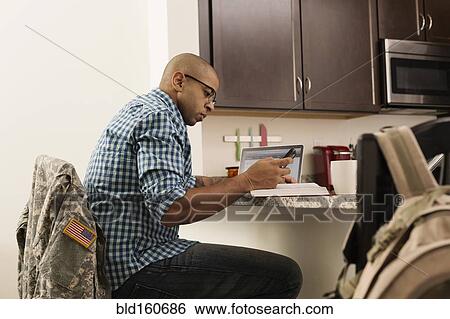 Stock Photograph - Mixed race soldier using laptop and cell phone on counter. Fotosearch