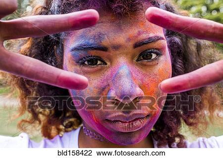 Stock Image - Mixed race woman covered in pigment powder gesturing peace signs. Fotosearch