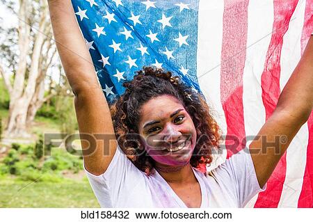 Stock Image - Mixed race woman covered in pigment powder holding American flag. Fotosearch