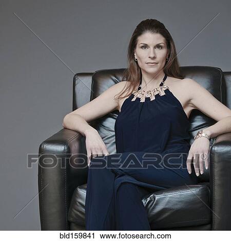 Stock Image - Mixed race woman in evening gown sitting in armchair. Fotosearch