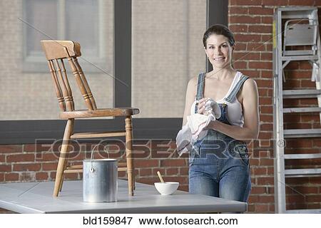 Stock Photo - Mixed race woman painting chair in loft. Fotosearch