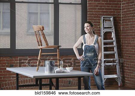 Stock Photograph - Mixed race woman painting chair in loft. Fotosearch