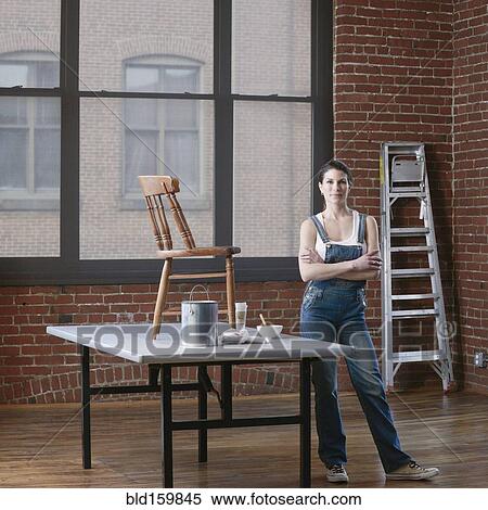 Stock Photography - Mixed race woman painting chair in loft. Fotosearch