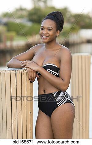 Stock Image - Mixed race woman wearing bikini leaning on post. Fotosearch