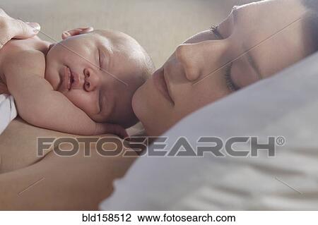 Stock Image - Mother sleeping with newborn baby on bed. Fotosearch