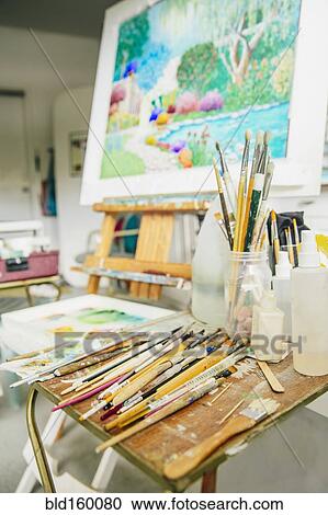 Stock Image - Paintbrushes, palette and easel with painting in studio. Fotosearch