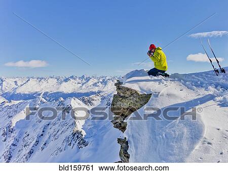 Stock Image - Photographer photographing from snowy mountaintop. Fotosearch
