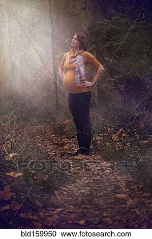 Stock Image - Pregnant Caucasian woman standing in forest. Fotosearch