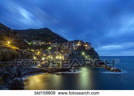 Stock Photo - Rocky Manarola coastline illuminated at night, La Spezia, Italy. Fotosearch