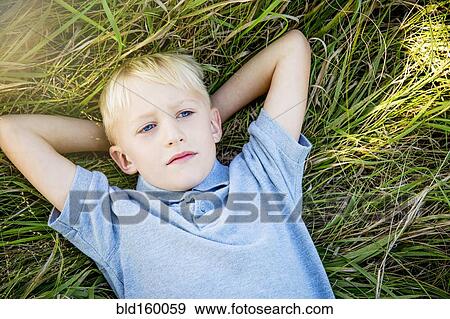 Stock Photo - Serious Caucasian boy laying in tall grass. Fotosearch
