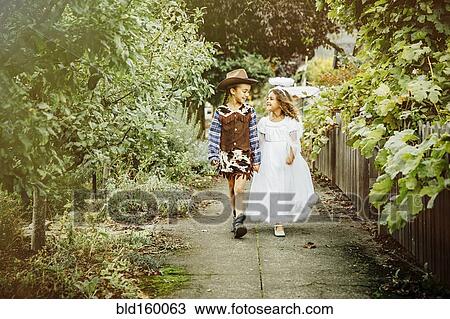 Stock Image - Sisters wearing Halloween costumes on sidewalk. Fotosearch