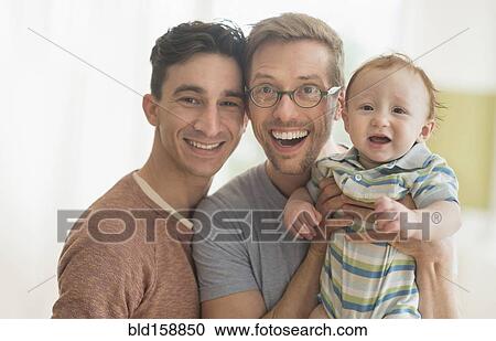 Stock Image - Smiling Caucasian gay fathers holding baby. Fotosearch