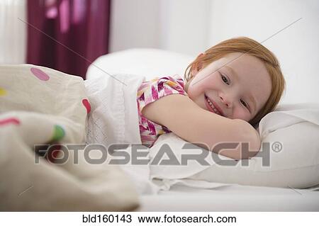 Stock Image - Smiling Caucasian girl laying in bed. Fotosearch