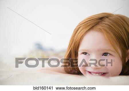 Stock Image - Smiling Caucasian girl laying on bed. Fotosearch