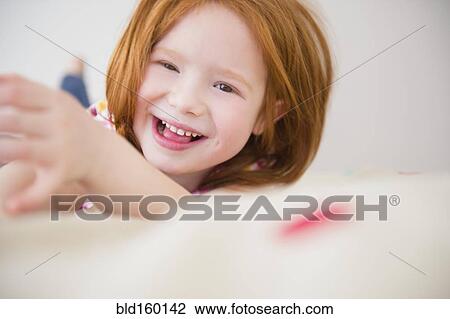 Stock Image - Smiling Caucasian girl laying on bed. Fotosearch