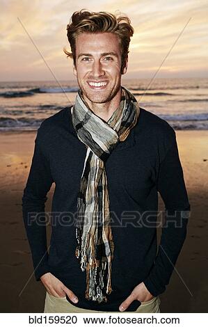 Stock Image - Smiling Caucasian man standing on beach. Fotosearch