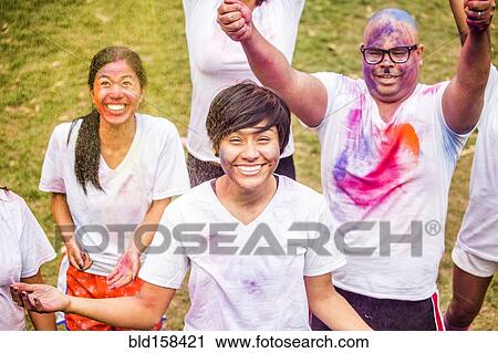 Stock Image - Smiling friends covered in pigment powder cheering. Fotosearch