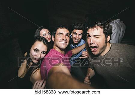 Stock Image - Smiling friends taking selfie in nightclub. Fotosearch