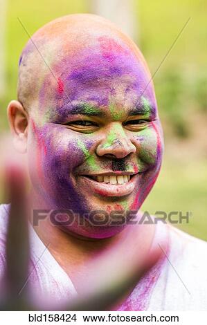 Picture - Smiling man covered in pigment powder gesturing peace sign, . Fotosearch