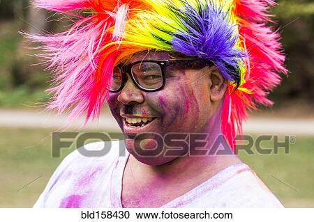 Stock Image - Smiling man covered in pigment powder wearing multicolor wig. Fotosearch