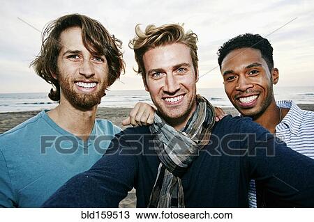 Stock Image - Smiling men taking selfie on beach. Fotosearch