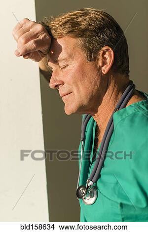 Picture - Stressed Caucasian nurse leaning on wall. Fotosearch