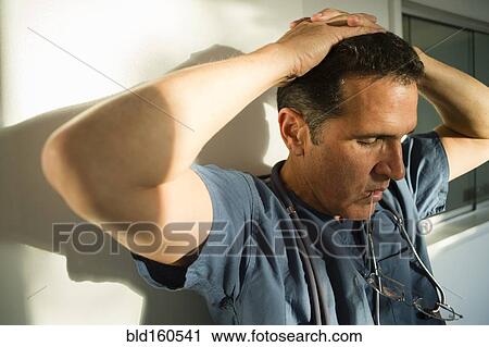 Stock Image - Stressed Hispanic doctor leaning on wall. Fotosearch