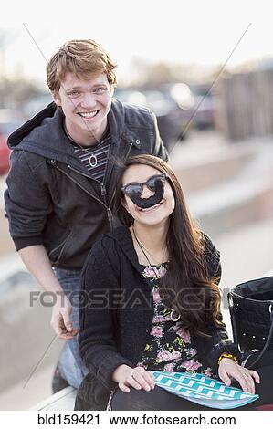 Stock Image - Teenage couple playing with fake mustache. Fotosearch