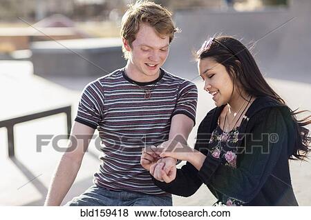 Stock Photo - Teenage girl tying bracelet around wrist of boyfriend. Fotosearch