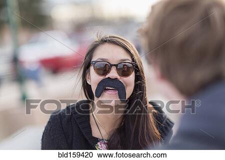 Stock Image - Teenage girl wearing fake mustache. Fotosearch