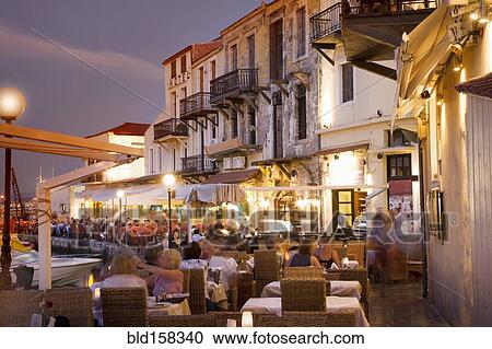 Stock Image - Time lapse view of sidewalk cafe at sunset, Mykonos, Cyclades, Greece. Fotosearch