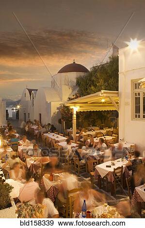 Stock Photo - Time lapse view of tourists eating in sidewalk cafe at sunset, Mykonos, Cyclades, Greece. Fotosearch