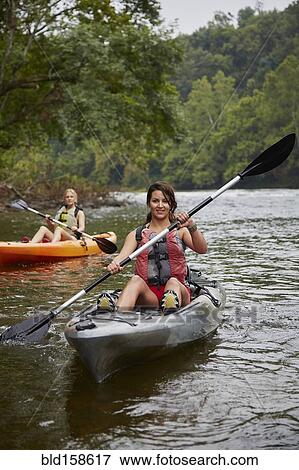 Stock Photo - Women paddling kayaks in remote river. Fotosearch