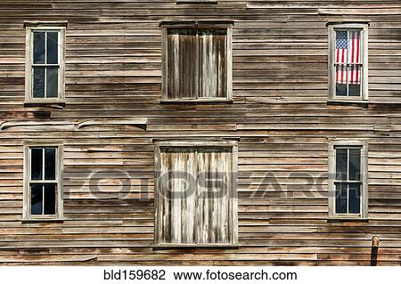 Stock Image - Wooden house exterior with American flag in window. Fotosearch