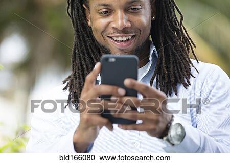 Stock Image - African American businessman using cell phone outdoors. Fotosearch