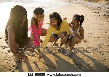Stock Photo - African American mother and daughters drawing on beach sand. Fotosearch