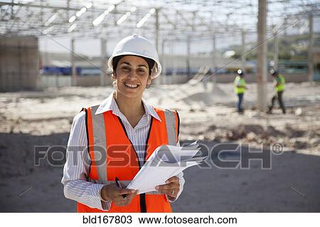Stock Image - Architect holding blueprints at construction site. Fotosearch