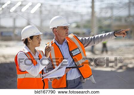 Architects reading blueprints at construction site View Large Photo Image Stock Image - Architects reading blueprints at construction site. Fotosearch