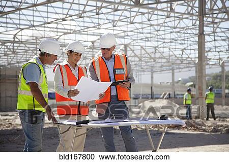 Architects reading blueprints at construction site View Large Photo Image Stock Image - Architects reading blueprints at construction site. Fotosearch
