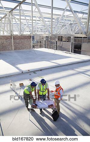 Stock Image - Architects reading blueprints at construction site. Fotosearch