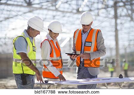 Stock Photo - Architects reading blueprints at construction site. Fotosearch