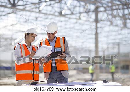 Stock Photo - Architects reading blueprints at construction site. Fotosearch
