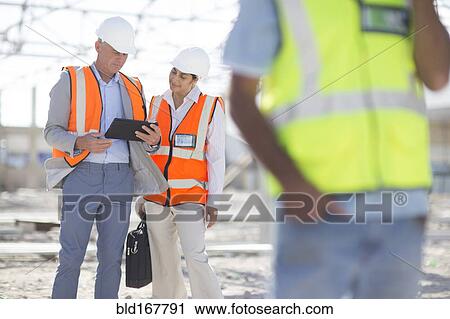 Stock Image - Architects using digital tablet at construction site. Fotosearch