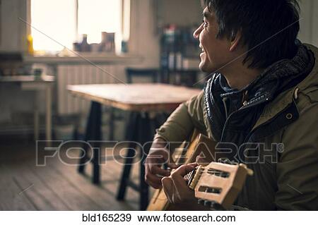 Stock Photo - Asian man playing guitar indoors. Fotosearch