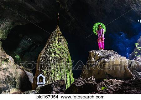 Picture - Asian woman standing on rock formation in cave temple. Fotosearch