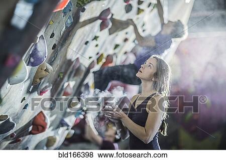 Stock Photo - Athlete chalking her hands at rock wall in gym. Fotosearch